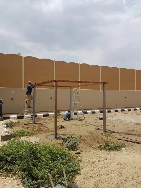 عمّال على سلالم يركّبون ساتر ألواح مقوّس في موقع عمل