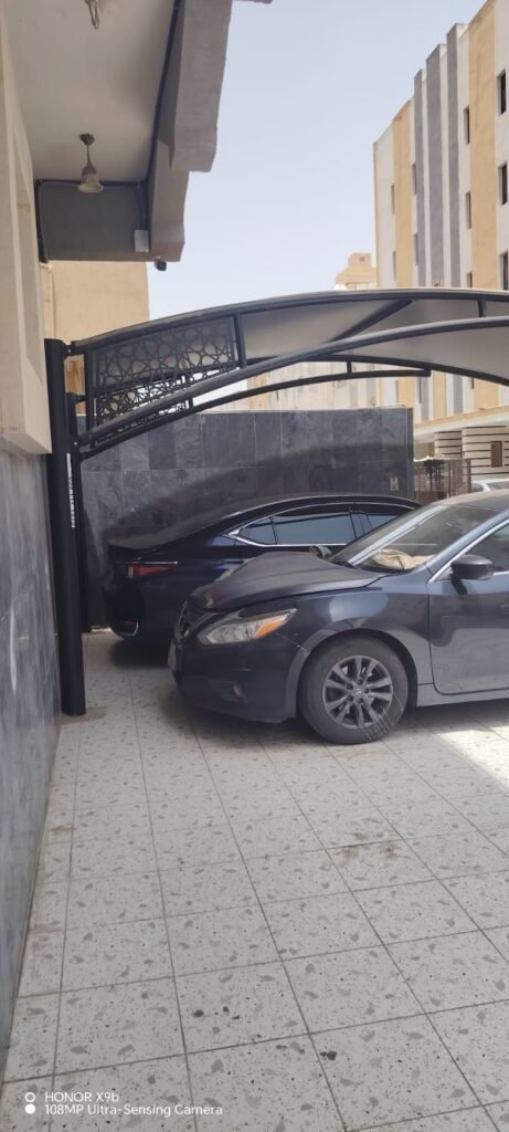 مظلة مقوّسة بحافة مزخرفة تغطي سيارات في ممر بين مبنيين