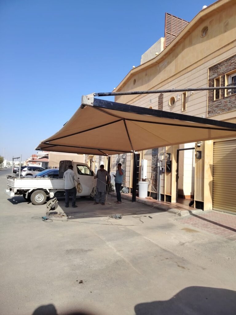 مظلة بتغطية فاتحة فوق حوش أثناء التركيب ويظهر فريق العمل وسيارة