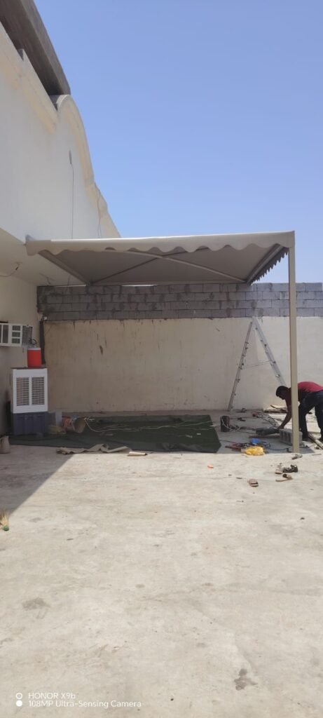 مظلة بتغطية فاتحة فوق حوش منزل أثناء التنفيذ ويظهر جدار بلوك وعامل