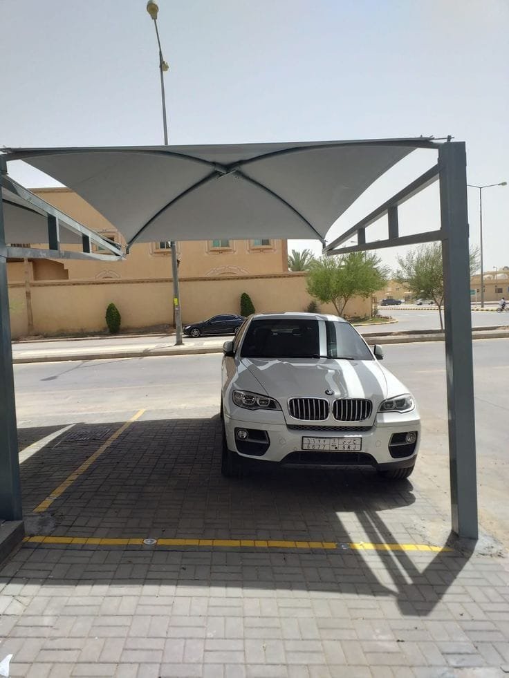 مظلة موقف بتغطية فاتحة على هيكل معدني داكن فوق سيارة واحدة في الشارع