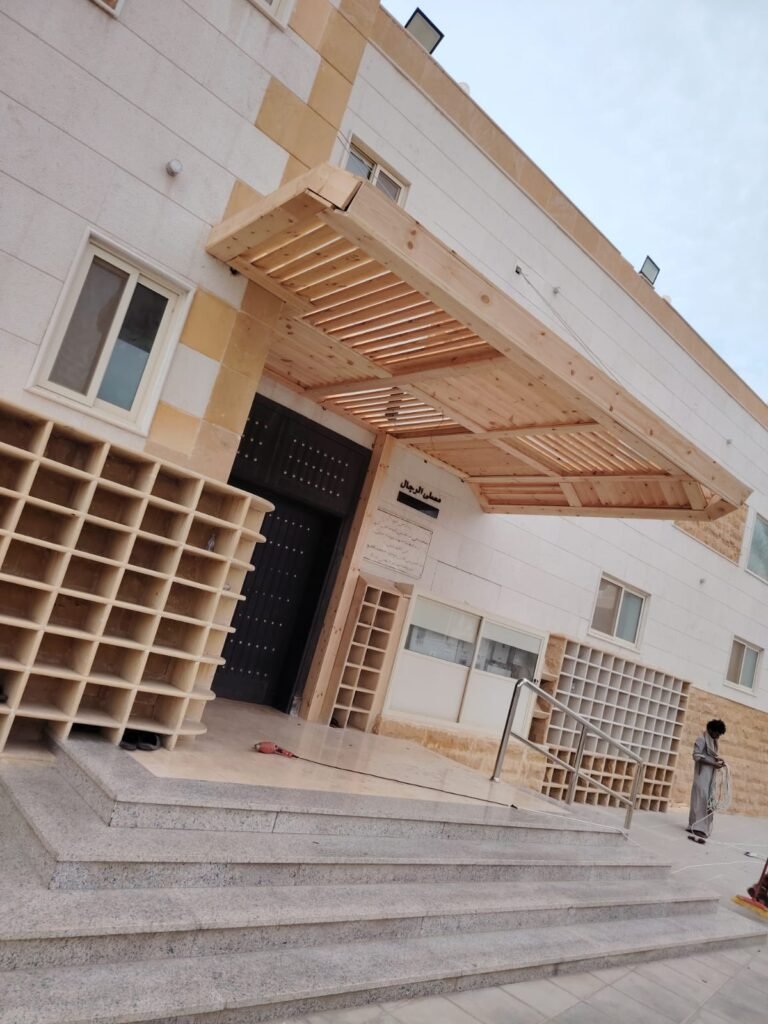 مظلة بشرائح خشبية المظهر فوق مدخل مبنى بواجهة حجرية ودرج