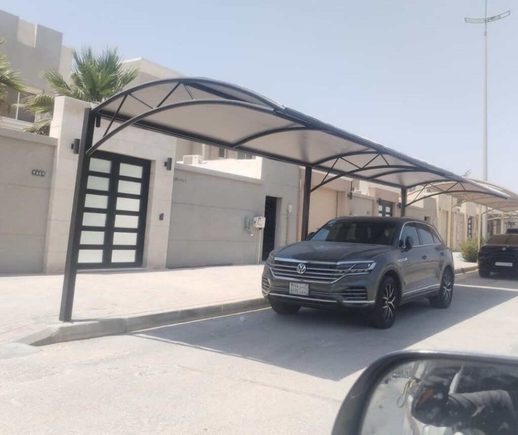 مظلة مقوّسة مزدوجة بتغطية فاتحة على هيكل داكن فوق ممر سيارات وسيارة أسفلها